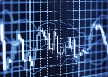 A blue-toned financial graph from advanced backtesting software shows fluctuating candlestick patterns and moving averages, indicating stock market or financial data trends. The graph features a grid background with various peaks and troughs, highlighting the volatility of the data. | FintechZoom