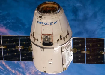 A white SpaceX Dragon spacecraft with solar panels extended floats in space against the backdrop of Earth and the upper atmosphere. Featuring prominent branding and detailed mechanical components, it embodies the optimistic market outlook for commercial space travel. | FintechZoom