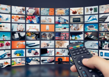A hand holds a TV remote pointed towards a curved screen displaying a grid of various multimedia thumbnails. The thumbnails include images of food, electronics, pets, and nature, representing a wide range of content to choose from on M4uHD. | FintechZoom