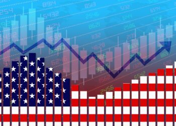 An illustration depicting a stock market chart overlaid with a U.S. flag-themed bar graph, symbolizing the U.S. economy. The background features a blue to red gradient with various stock numbers and candlestick chart patterns, and a line graph showing fluctuating market trends. | FintechZoom