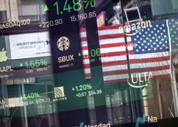 A digital display shows Stock Market Today information, including companies like Starbucks (SBUX), Apple (AAPL), United Airlines, Amazon, and Ulta Beauty. The American flag is reflected in the background, symbolizing the U.S. financial market. | FintechZoom