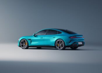 A sleek, turquoise electric sedan with a modern design, showcasing its luxurious style and aerodynamic shape. The car features dark-tinted windows, multi-spoke alloy wheels, and is parked in a minimalist, grey studio setting—a scene as cutting-edge as Xiaomi stock trends. | FintechZoom