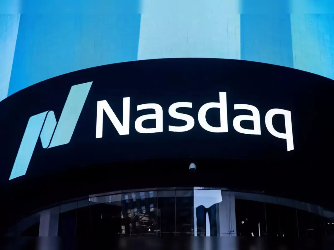A large, curved screen displays the Nasdaq FintechZoom logo with white letters and a stylized blue "N" on a black background. The screen is situated above the entrance to a building, reflecting the skyline. The image is captured during the daytime. | FintechZoom