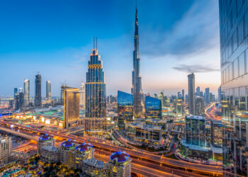A stunning cityscape of Dubai at dusk featuring the Burj Khalifa prominently in the center. The skyline, marked with numerous high-rise buildings and intricate roadways, is starting to illuminate. Reflecting modern architecture and vibrant city life, it symbolizes both innovation and opportunities for halal investments. | FintechZoom