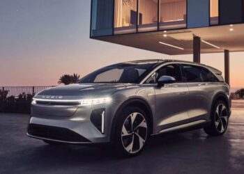 A sleek, silver Lucid electric SUV is parked in front of a modern house with large windows during sunset. The vehicle features distinctive LED headlights and aerodynamic design, positioned on a stylish driveway with a scenic view in the background—an embodiment of where Lucid (LCID) stock potential shines. | FintechZoom