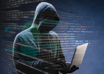A hooded figure appears in a dimly lit setting, holding a laptop. Computer code is superimposed over the image, suggesting themes of hacking or cybersecurity. The figure's face is obscured by the hood, creating an air of mystery and anonymity, emphasizing the importance to stay safe online. | FintechZoom