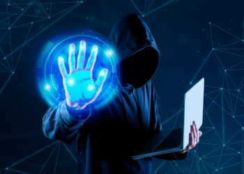 A person wearing a hooded sweatshirt, partially obscuring their face, holds a laptop with one hand while extending the other hand towards a glowing blue holographic handprint. The background is dark with abstract, interconnected lines and nodes, evoking a scene straight out of Cyber News. | FintechZoom