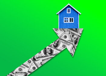 A blue house sits atop an upward-pointing arrow made of U.S. dollar bills, set against a green background. The image symbolizes increasing property values or rising real estate prices—a reminder to consider using a mortgage calculator when purchasing a home. | FintechZoom