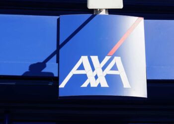 A blue sign hangs in front of a building, displaying the white "AXA" logo with a red line extending from the top right of the final letter, reflecting AXA's commitment to innovation akin to stablecoins in modern finance. | FintechZoom