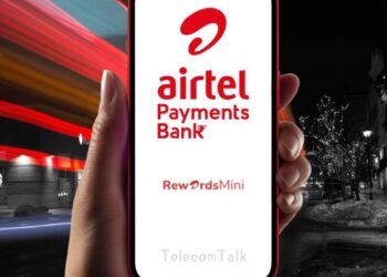 A hand holds a smartphone displaying the Airtel Payments Bank logo with the text "Airtel Payments Bank" and "RewardsMini." The background captures city street lights at night, blending red and white light streaks, while an Airtel Payment Bank IFSC Code subtly appears beneath the logo. | FintechZoom