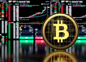 A shiny gold Bitcoin coin with the "B" symbol stands prominently in the foreground. In the background, multiple digital trading charts and graphs are displayed on screens, showcasing market data and cryptocurrency trends from CryptoNewzHub.com. | FintechZoom