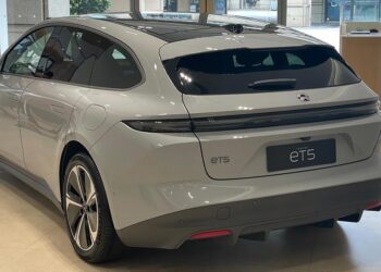 A sleek, modern silver-grey sedan, the NIO ET5, is parked in a well-lit showroom. The car features smooth, aerodynamic lines, tinted windows, and a panoramic sunroof. The NIO logo is prominently displayed on the rear—a testament to the rising acclaim of NIO stock in the automotive market. | FintechZoom