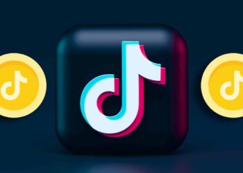 A 3D TikTok logo with its distinctive musical note design is centered against a dark blue background. Flanked by two yellow coins, each featuring the TikTok logo, this vibrant scene captures the essence of TikTok Coins Recharge, adding dynamic and engaging visual appeal. | FintechZoom