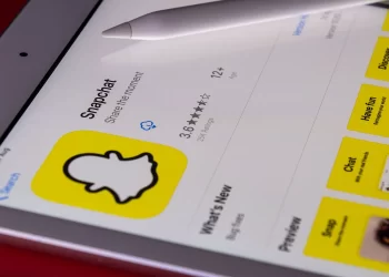 A tablet screen displays the Snapchat app page on the App Store, showcasing the app's logo, description, and rating of 3.6 stars with over 225K ratings. A stylus rests on top of the screen, hinting at exploring Snapchat Premium Features. | FintechZoom