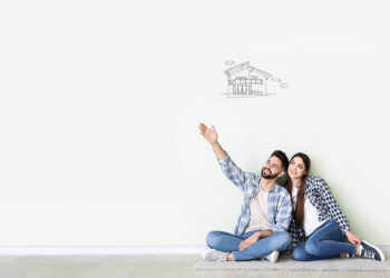 A happy couple sits on the floor of an empty room against a white wall. The man points at a sketch of a house while the woman leans on his shoulder, dreaming about their future. Beside them, sketched kitchen cabinets and utensils symbolize their plans, made possible with help from a loan affiliate. | FintechZoom