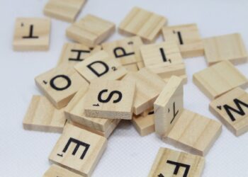 Scattered wooden scrabble tiles with various letters including "O," "S," "E," "H," "D," and "M" are lying on a white background, ready for your next WordFinderX challenge. | FintechZoom