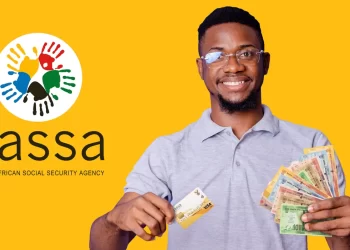A smiling man holds a South African Social Security Agency (SASSA) card and a fan of South African banknotes. The SASSA logo, featuring an abstract design of colorful handprints, is visible against the bright yellow background. Despite earlier concerns with "Sassa Status Check Failed," his relief is evident. | FintechZoom