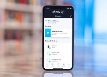 A smartphone displays the Xfinity xFi app. The screen shows network information, including network name, security status indicating "Advanced Security," and the status of connected devices such as a Gateway, Upstairs Pod, and Living Room Pod. Easily manage this alongside your Comcast Email Login for seamless connectivity. | FintechZoom