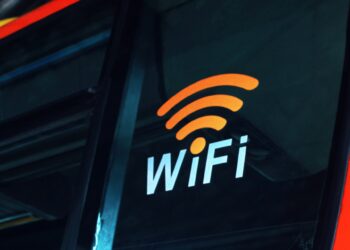 Image of a "WiFi" sign in bold white letters accompanied by an orange wireless signal icon, displayed on the window of a vehicle. The background is slightly blurred, suggesting motion, reminiscent of accessing 10.0.0.1 for Piso Wifi Pause settings while on the go. | FintechZoom