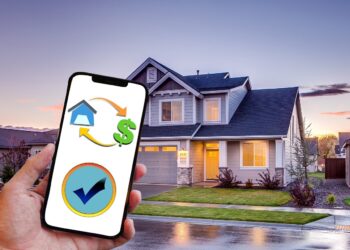 A person holds a smartphone in front of a modern suburban house at dusk. The phone screen displays icons of a house, dollar sign, and a checkmark, suggesting apps related to the mortgage industry or financial transactions for home buying or selling. | FintechZoom