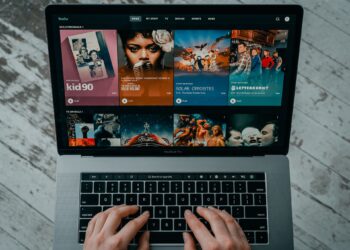 A person is typing on a MacBook Pro displaying the Hulu streaming service interface. Various TV show and movie thumbnails are visible on the screen, including titles such as "kid90," "Soul of a Nation," and "Solar Opposites." It’s reminiscent of browsing through Watch32 for endless entertainment options. | FintechZoom