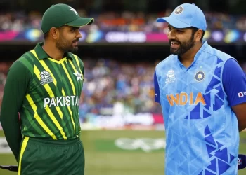 Two cricketers stand on a field, engaged in conversation. One wears a green and yellow Pakistan uniform, while the other is in a blue and orange India uniform. A crowd in the background suggests it's an exciting India vs Pakistan Asia Cup 2023 match setting. | FintechZoom