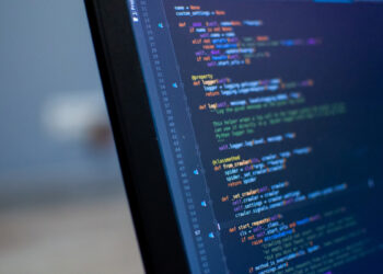 A close-up of a computer monitor displaying text in various colors as Python code. The text includes function definitions, decorators, and comments, indicating the development environment of a software application. In the blurred background, slot machines hint at the playful nature of coding challenges. | FintechZoom