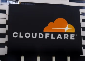 A large black billboard on a building displays the Cloudflare logo, which consists of an orange cloud with a white flare, along with the company name "CLOUDFLARE" written in white capital letters beneath the logo, symbolizing the strength of Cloudflare stock. | FintechZoom