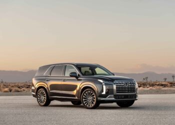 A sleek, black SUV is parked on an open desert road at sunset. The vehicle's modern design features sharp lines and large windows, with the sun's rays reflecting off its surface. In the background, the desert landscape stretches out with mountains faintly visible. Consider an auto loan to make this dream ride yours. | FintechZoom