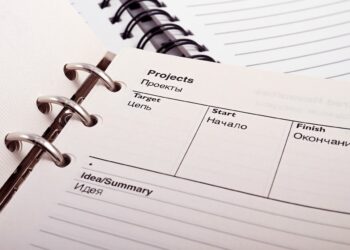 A close-up of an open planner with text in both English and Russian. The sections visible include "Projects," "Target," "Start," "Finish," and "Idea/Summary." The planner has a spiral binding with some blank lined pages in the background. | FintechZoom