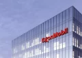 A modern glass office building with the ExxonMobil logo prominently displayed in red letters near the top corner stands against a backdrop of a slightly cloudy sky, reflecting the steady performance of Exxon Mobil stock. | FintechZoom