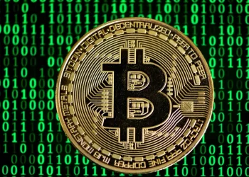 A gold Bitcoin coin with the letter "B" symbol at the center, featuring intricate engravings and binary code patterns. The background is filled with a green matrix-style digital binary code pattern, emphasizing the digital and technological aspect of cryptocurrency, making it a unique visual statement to invest in Bitcoin. | FintechZoom