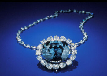 A stunning necklace featuring a deep blue gemstone surrounded by a halo of sparkling white diamonds. The blue gem is the focal point, attached to a chain adorned with more diamonds, set against a rich blue background—an ideal choice for those investing in jewelry. | FintechZoom