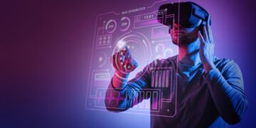 A person wearing a virtual reality headset interacts with a holographic interface. The background is a gradient of purple and blue, enhancing the futuristic tech ambiance with icons, graphs, and data displayed in vivid detail. | FintechZoom