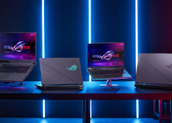 A row of four ASUS ROG laptops, touted as the best gaming laptops, is displayed on a table against a backdrop of blue and red vertical neon lights. The laptops are open, showcasing futuristic screens with the ROG logo. The ambient light creates a high-tech, gaming atmosphere. | FintechZoom
