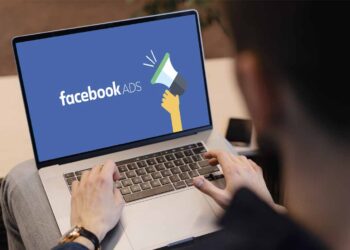 A person is typing on a laptop that prominently displays the Facebook Ads logo, which features the text "facebook ADS" next to an illustration of a hand holding a megaphone. | FintechZoom