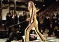 A person in a yellow tracksuit stands confidently with a sword in hand, reminiscent of one of the best movies on Netflix, surrounded by multiple individuals in black suits with blindfolds. They appear to have been defeated in combat, either lying on the ground or posed defensively, within a traditional interior setting. | FintechZoom
