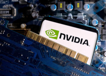 A close-up image showcasing a Nvidia logo on a smartphone screen. The phone is positioned against a computer motherboard and a blue circuit board with visible gold connectors, emphasizing technology and connectivity themes, subtly hinting at the recent Nvidia stock split. | FintechZoom