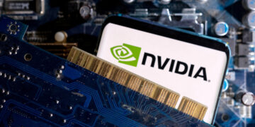 A close-up image showcasing a Nvidia logo on a smartphone screen. The phone is positioned against a computer motherboard and a blue circuit board with visible gold connectors, emphasizing technology and connectivity themes, subtly hinting at the recent Nvidia stock split. | FintechZoom