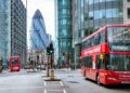Busy London street with red double-decker buses, including one displaying route 205 to Paddington. Modern skyscrapers like the Gherkin tower in the background. Amidst discussions about the UK interest rate, people walk on sidewalks and cross streets, capturing everyday city life. | FintechZoom