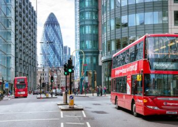 Busy London street with red double-decker buses, including one displaying route 205 to Paddington. Modern skyscrapers like the Gherkin tower in the background. Amidst discussions about the UK interest rate, people walk on sidewalks and cross streets, capturing everyday city life. | FintechZoom