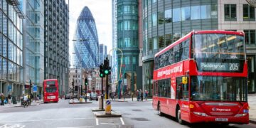 Busy London street with red double-decker buses, including one displaying route 205 to Paddington. Modern skyscrapers like the Gherkin tower in the background. Amidst discussions about the UK interest rate, people walk on sidewalks and cross streets, capturing everyday city life. | FintechZoom