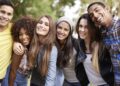 A group of six young adults stands close together outdoors, smiling at the camera. Casually dressed with lush greenery in the background, they appear to be enjoying each other's company and discussing their favorite topics on a sunny day, possibly even sharing tips about the best student credit cards. | FintechZoom