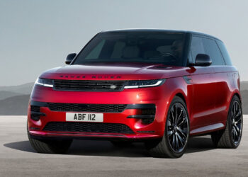 A vibrant red Range Rover SUV, possibly the best hybrid SUV on the market, is parked on a plain concrete surface, set against a backdrop of hazy mountains and a clear sky. The vehicle features sleek, modern design elements with black detailing around the windows, grille, and wheels. The license plate reads "ABF 112. | FintechZoom