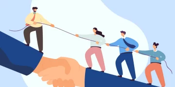 Illustration of four people pulling on a rope, seemingly in a tug-of-war. They are depicted standing on an enlarged handshake, symbolizing team building activities and unity. The background is a light blue with abstract shapes. | FintechZoom