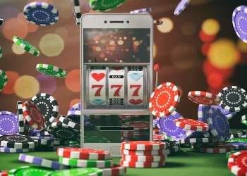A smartphone displaying a slot machine with "777" on the screen sits among scattered poker chips of various colors, including red, blue, black, green, and white. The background is blurred with colorful bokeh lights, creating a festive casino-like atmosphere perfect for playing online slots. | FintechZoom