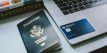 Close-up of a desk with a United States passport, the best travel credit card—Chase Sapphire Preferred—and an open laptop. Part of a book is visible in the corner, titled "ROUTE." The passport is slightly worn, while the card and laptop are in good condition. | FintechZoom