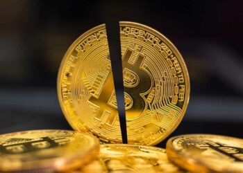 A close-up of three gold-colored Bitcoin tokens placed on a dark surface. The center token is prominently displayed with a vertical black line bisecting it, symbolizing the concept of a Bitcoin halving event, which often impacts the Bitcoin price. The iconic Bitcoin logo is clearly visible. | FintechZoom