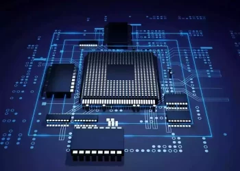 A 3D-rendered image of a computer chip, symbolizing the booming chip stocks up market, surrounded by other microchip components on a dark, illuminated circuit board. Blue lines and dots represent electronic pathways, creating a high-tech, futuristic appearance. The background is deep blue and black. | FintechZoom