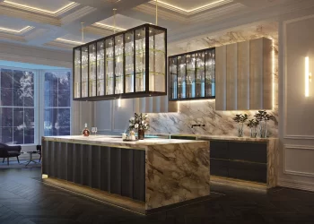 A luxurious modern kitchen with marble countertops and island, a glass rack above the island, and sleek dark wood cabinets. The room features elegant lighting, glass kitchen splashbacks, a large window with a tranquil view, and a cozy seating area with an armchair in the corner. | FintechZoom